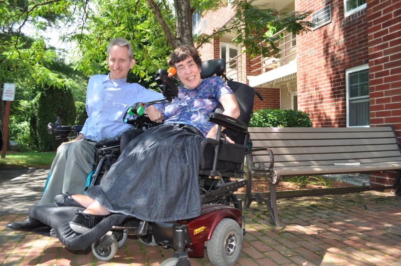 Residents in motorized wheel chairs, smiling in front of building